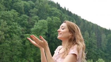 Kırmızı manikür ve pembe elbise ile Genç çekici sarışın kız yeşil orman arka plan ile dağ üzerinde soğuk bahar veya sonbahar yağmur altında duruyor.