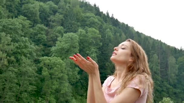 Giovane attraente ragazza bionda con manicure rossa e abito rosa è in piedi sotto la fredda primavera o autunno pioggia sopra la montagna con sfondo verde foresta . — Video Stock