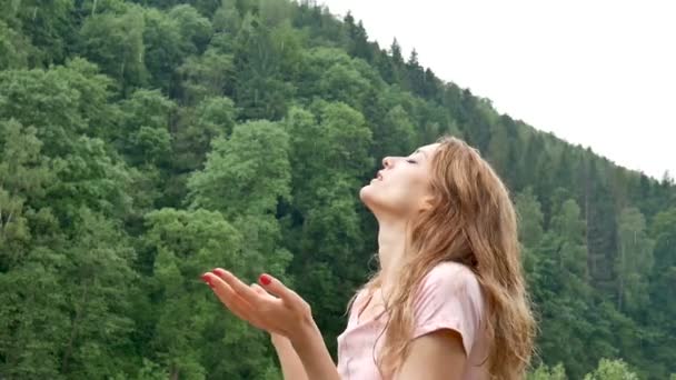 Junge Frau mit blonden Haaren und roter Maniküre im Freien bei regnerischem Wetter ohne Regenschirm über Berg mit grünem Waldhintergrund. — Stockvideo