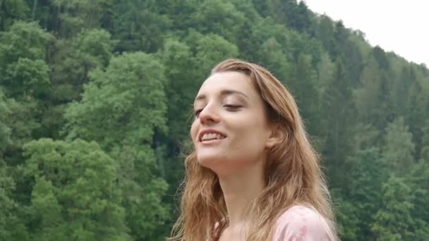 Mujer joven con cabello rubio y manicura roja al aire libre en clima lluvioso sin paraguas sobre la montaña con fondo verde del bosque . — Vídeos de Stock