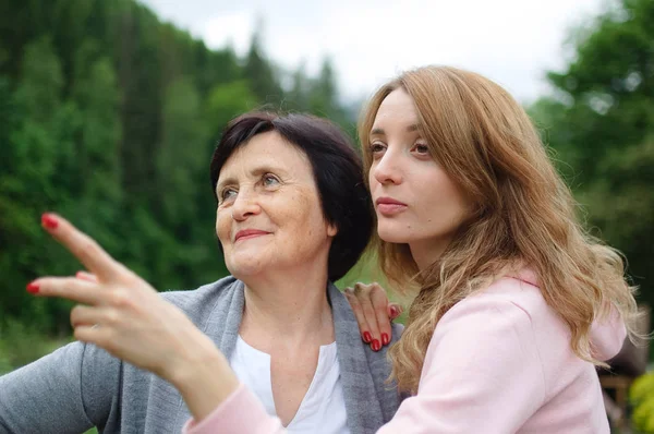 Happy senior woman with short dark hair and wrinkles on her face spending time together with her adult daughter, young girl is pointing at something. Concept of travelling with family — Stock Photo, Image