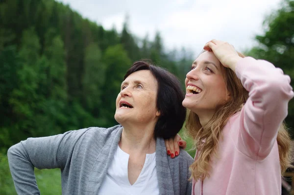 La madre y su hija adulta están viajando y posando juntas sobre un paisaje de bosque y montañas. Concepto de ternura, cuidado, amor familiar, relaciones . —  Fotos de Stock