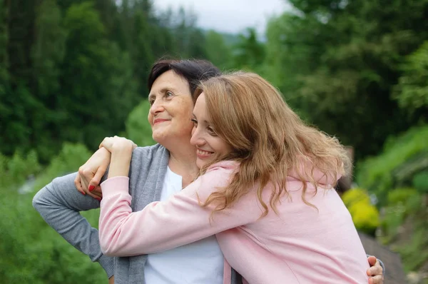 La madre y su hija adulta están abrazando pasar tiempo juntos al aire libre sobre el paisaje de bosque y montañas. Concepto de ternura, cuidado, amor familiar, relaciones . —  Fotos de Stock