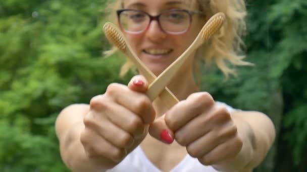 Joven chica hermosa con cola de caballo está sosteniendo un cepillo de dientes de bambú útil al aire libre durante el tiempo lluvioso en el fondo del árbol verde. Adecuación al medio ambiente y concepto cero residuos . — Vídeos de Stock