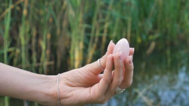 Nehir arka planda bir gül kuvars kristal Yoni yumurta tutan kadın el. Kadın sağlığı, doğa konseptleri ile birlik