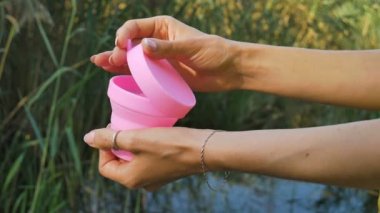 Kadın elleri göl ile yeşil doğal arka plan üzerinde duran pembe silikon adet fincan nasıl kullanılacağını gösteriyor. Kadın sağlığı kavramı, sıfır atık alternatifleri