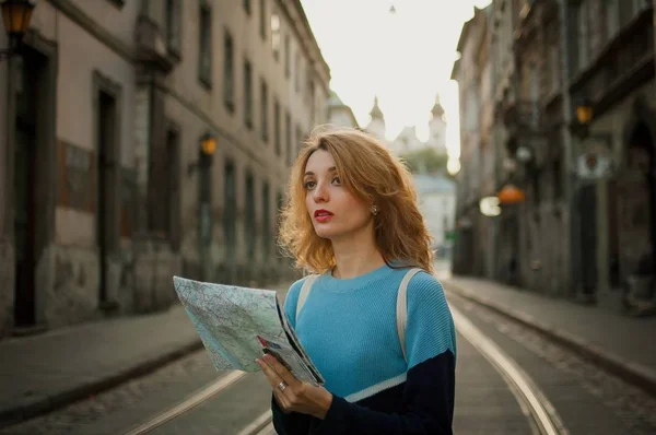 Молодая женщина смотрит на бумажную карту и ищет направление рано утром в древнем европейском городе на пустой улице с трамвайным фоном — стоковое фото