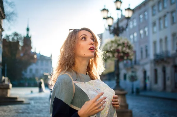 Menina adulta feliz animado está olhando para o mapa de papel e à procura de direção no início da manhã na antiga cidade europeia na praça vazia — Fotografia de Stock