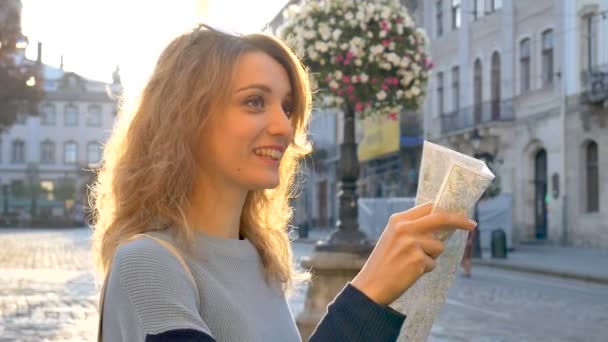 Szczęśliwy podekscytowany dziewczyna dorosłych patrzy na mapie papierowej i poszukiwania kierunku wcześnie rano w starożytnym europejskim mieście na pustym placu — Wideo stockowe