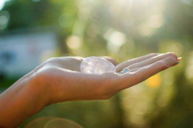 Vumfit, imbuilding veya meditasyon için şeffaf ametist kuvars yoni yumurta ile Kadın el. Gökyüzü ve gündoğumu arka plan açık havada ellerde parlayan kristal yumurta. Kadın sağlığı kavramı.