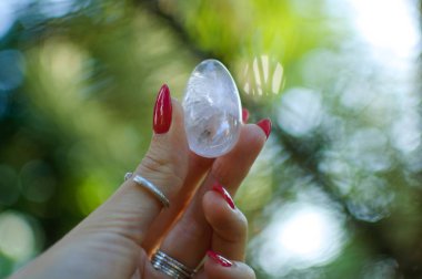 Vumfit, imbuilding veya meditasyon için şeffaf ametist kuvars yoni yumurta ile Kadın el. Gökyüzü ve gündoğumu arka plan açık havada ellerde parlayan kristal yumurta. Kadın sağlığı kavramı.