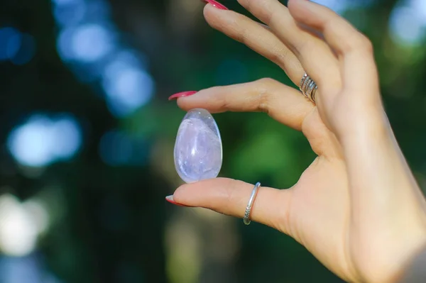 Mano femminile con uovo di yoni di quarzo ametista trasparente per vumfit, imbuilding o meditazione. Uovo di cristallo lucente in mani su cielo e sfondo di alba all'aperto. Concetto di salute delle donne . — Foto Stock