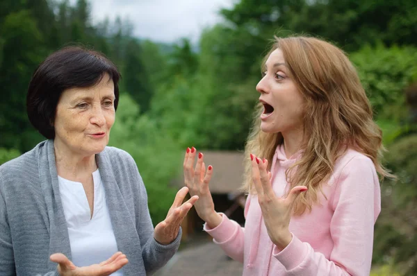 Outdoors portrait of senior mother and adult daughter are communicating outside over landscape of forest and mountains. Two generations, problems between children and parents concept — Stock Photo, Image