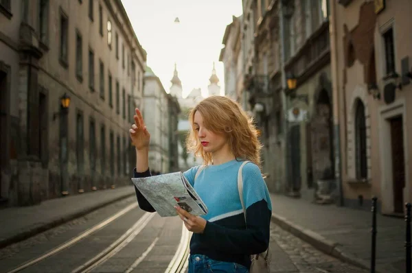 Jovem mulher olhando para o mapa de papel e procurando direção no início da manhã na antiga cidade europeia na rua vazia com fundo de bonde — Fotografia de Stock