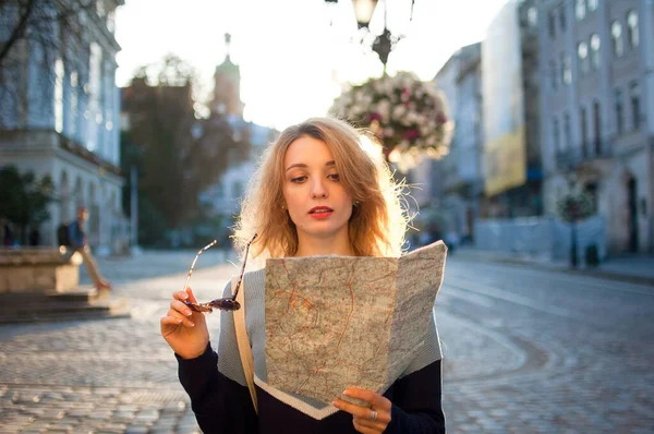 Retrato feminino de uma turista mulher com óculos de sol e mapa de papel em suas mãos em busca de direção no início da manhã na praça antiga vazia — Fotografia de Stock