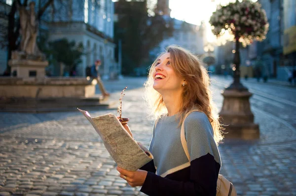 Menina adulta feliz animado está olhando para o mapa de papel e à procura de direção no início da manhã na antiga cidade europeia na praça vazia — Fotografia de Stock