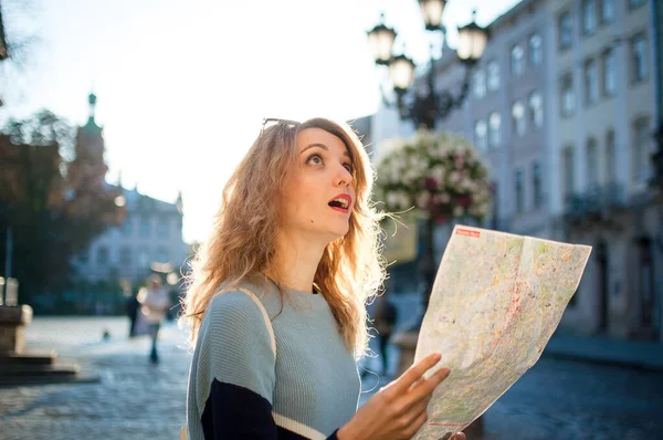 Menina adulta feliz animado está olhando para o mapa de papel e à procura de direção no início da manhã na antiga cidade europeia na praça vazia — Fotografia de Stock