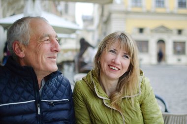 Yakışıklı yaşlı adam, genç sarışın karısını kucaklıyor. Baharın başında ya da sonbaharda antik şehirde birlikte vakit geçiriyorlar..