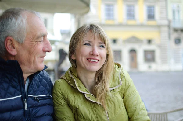 Hombre mayor guapo está abrazando a su joven esposa rubia pasar tiempo juntos al aire libre en la ciudad antigua durante principios de primavera u otoño . — Foto de Stock