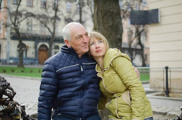 Snygg äldre man omfamnar sin unga blonda fru tillbringa tid utomhus i den antika staden under tidig vår eller höst. — Stockfoto