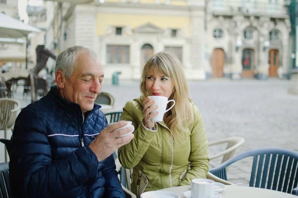 Retrato de casal romântico feliz com diferença de idade beber café no café com terraço ao ar livre na cidade antiga pela manhã durante o início da primavera ou outono . — Fotografia de Stock