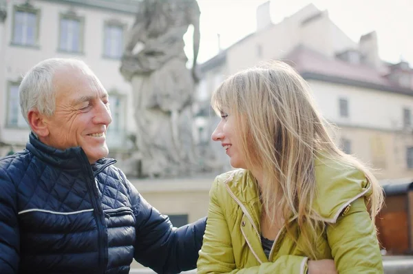 Hombre mayor guapo está abrazando a su joven esposa rubia pasar tiempo juntos al aire libre en la ciudad antigua durante principios de primavera u otoño . — Foto de Stock