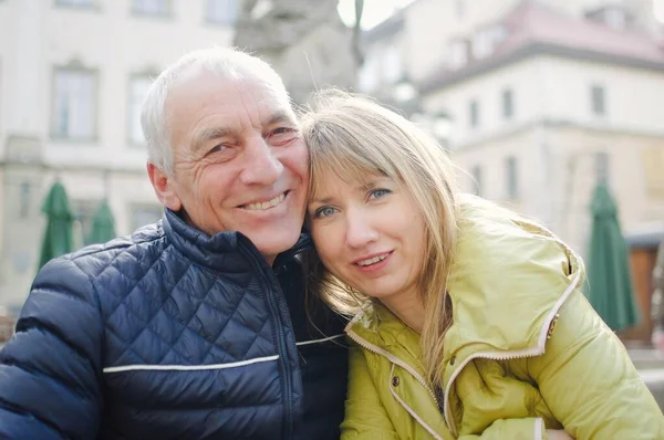Hombre mayor guapo está abrazando a su joven esposa rubia pasar tiempo juntos al aire libre en la ciudad antigua durante principios de primavera u otoño . —  Fotos de Stock
