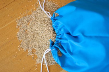 Ahşap arka plan üzerinde şeffaf mavi yeniden kullanılabilir çanta beyaz Quinoa tohumları. Vejetaryen gıda kavramı