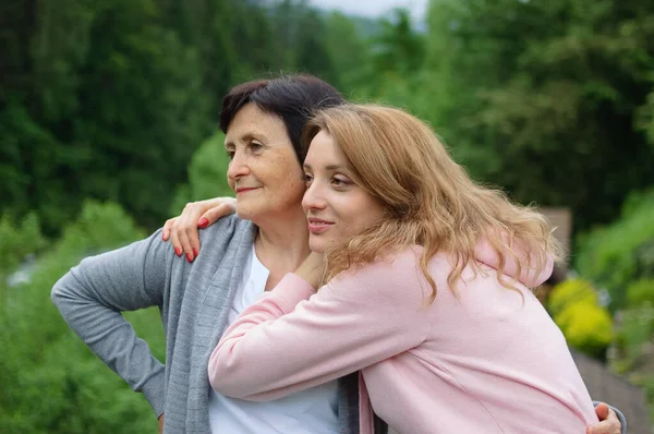 La madre y su hija adulta están abrazando pasar tiempo juntos al aire libre sobre el paisaje de bosque y montañas. Concepto de ternura, cuidado, amor familiar, relaciones . —  Fotos de Stock