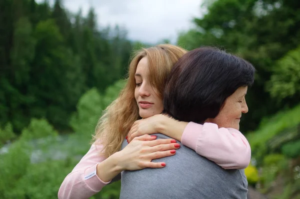 Mujer rubia joven está abrazando a su madre mayor disfrutando de estar juntos en las montañas durante las vacaciones. Concepto de ternura, cuidado, amor familiar, relaciones . —  Fotos de Stock