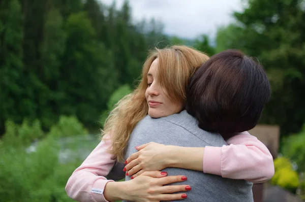 Mujer rubia joven está abrazando a su madre mayor disfrutando de estar juntos en las montañas durante las vacaciones. Concepto de ternura, cuidado, amor familiar, relaciones . —  Fotos de Stock