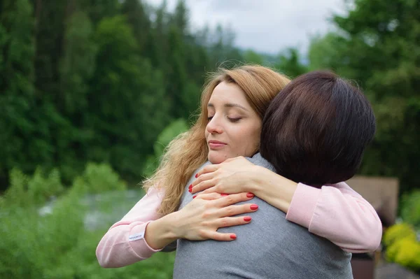 Mujer rubia joven está abrazando a su madre mayor disfrutando de estar juntos en las montañas durante las vacaciones. Concepto de ternura, cuidado, amor familiar, relaciones . —  Fotos de Stock