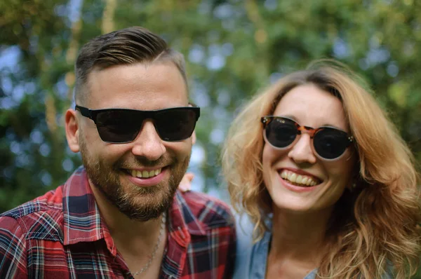 Primer plano retrato de pareja joven en gafas de sol mirando a la cámara sobre los árboles verdes de fondo, hipsters concepto — Foto de Stock