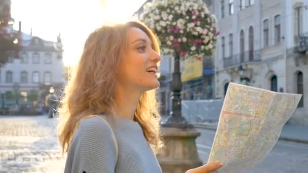 Feliz chica adulta emocionada está mirando el mapa de papel y en busca de dirección temprano en la mañana en la antigua ciudad europea en la plaza vacía — Vídeos de Stock