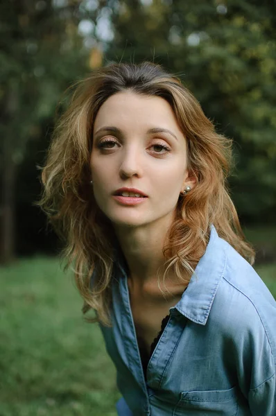 Ragazza bionda che indossa blu casual jeans camicetta sta guardando la fotocamera nel parco su sfondo alberi verdi — Foto Stock