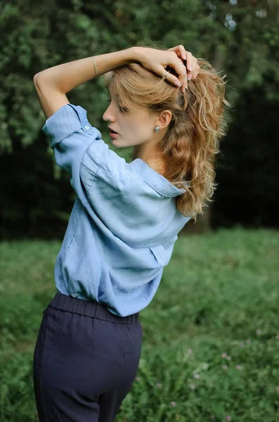 Voltar ver retrato de menina loira sexy com cabelo encaracolado vestindo azul casual jeans blusa posando no parque em árvores verdes fundo. Conceito de estilo Hipster . — Fotografia de Stock