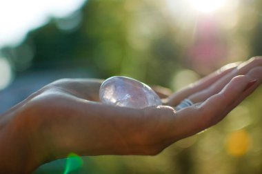 Vumfit, imbuilding veya meditasyon için şeffaf ametist kuvars yoni yumurta ile Kadın el. Gökyüzü ve gündoğumu arka plan açık havada ellerde parlayan kristal yumurta. Kadın sağlığı kavramı.