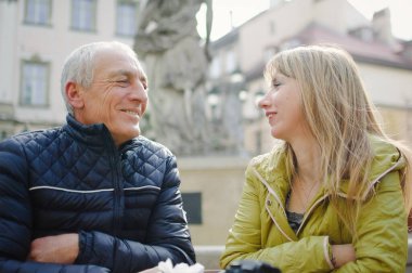 Yakışıklı yaşlı adam, genç sarışın karısını kucaklıyor. Baharın başında ya da sonbaharda antik şehirde birlikte vakit geçiriyorlar..