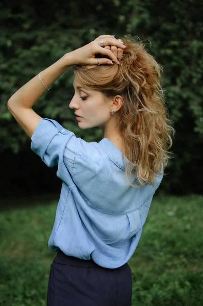 Voltar ver retrato de menina loira sexy com cabelo encaracolado vestindo azul casual jeans blusa posando no parque em árvores verdes fundo. Conceito de estilo Hipster . — Fotografia de Stock