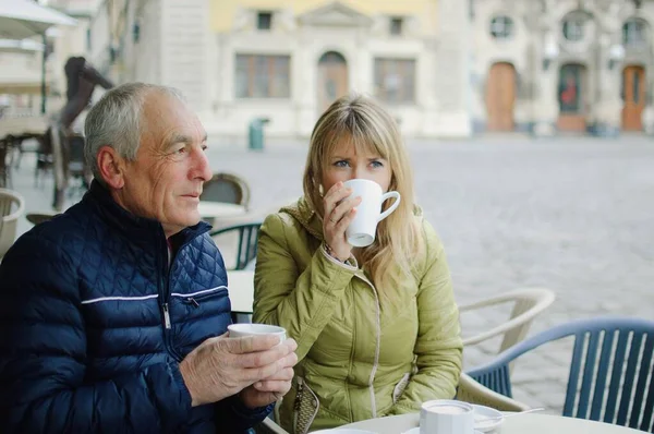 Retrato de casal romântico feliz com diferença de idade beber café no café com terraço ao ar livre na cidade antiga pela manhã durante o início da primavera ou outono . — Fotografia de Stock