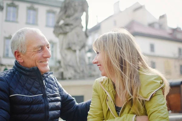 Hombre mayor guapo está abrazando a su joven esposa rubia pasar tiempo juntos al aire libre en la ciudad antigua durante principios de primavera u otoño . —  Fotos de Stock