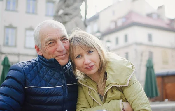 Snygg äldre man omfamnar sin unga blonda fru tillbringa tid utomhus i den antika staden under tidig vår eller höst. — Stockfoto