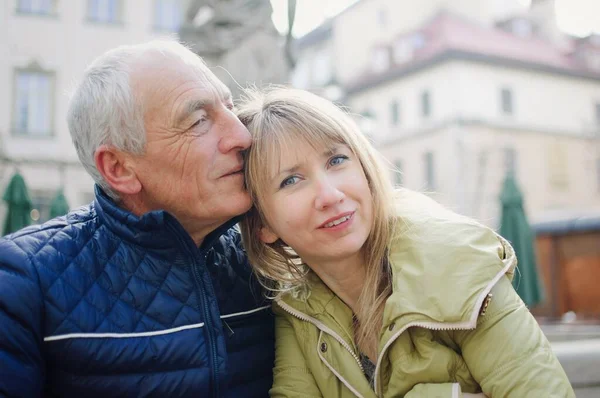 Hombre mayor guapo está abrazando a su joven esposa rubia pasar tiempo juntos al aire libre en la ciudad antigua durante principios de primavera u otoño . — Foto de Stock