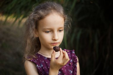 Parkta çikolata yiyen at kuyruklu ve menekşe elbiseli şirin sarışın kız. Gün boyu çikolata yiyor. Sağlıksız yaşam tarzı kavramı.