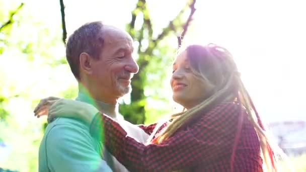 Die erwachsene Tochter mit ihrem älteren Vater beim Umarmen im Park an einem sonnigen Tag. Vatertagskonzept — Stockvideo