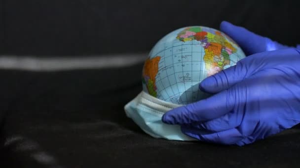 ウクライナのキリル文字で地理的な名前を持つ地球の地球は、保護手袋の医療の手の外科用マスクに身を包んだ上で。世界のコロナウイルス流行 — ストック動画