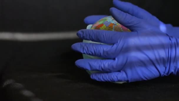 Земной шар с географическими названиями украинскими кириллическими буквами на нем одет в хирургическую маску в руках медика в защитных перчатках. Эпидемия коронавируса в мире — стоковое видео