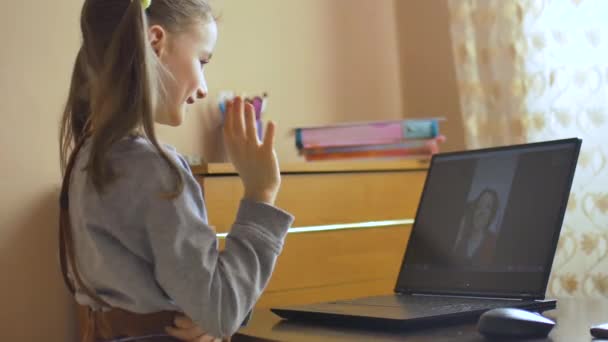 Vista posterior de la niña con dos colas de caballo diciendo hola para su tutor utilizando la cámara web de vídeo en el ordenador portátil negro en casa debido al auto-aislamiento debido a Coronavirus Covid-19. Educación remota — Vídeos de Stock