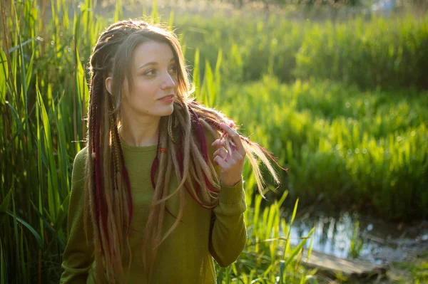 Buiten portret van een meisje met dreadlocks en groen shirt in een stadspark in de buurt van het meer tijdens een zonsondergang, wees vrij concept. — Stockfoto