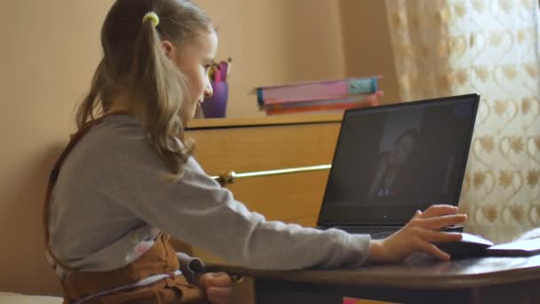 Rückansicht eines kleinen Mädchens mit zwei Pferdeschwänzen, das vor dem Bildschirm ihres schwarzen Laptops sitzt und wegen der Selbstisolation durch Coronavirus Covid-19 zu Hause bei ihrem Lehrer lernt. — Stockvideo
